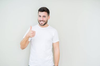 Hareketi el ile mutlu yaşasın yapıyor izole arka plan üzerinde rahat beyaz t-shirt giyen genç yakışıklı adam. Başarı gösteren kameraya bakarak ifade onaylama.