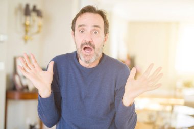 Yakışıklı orta yaş adam ev clueless ve şaşkın bir ifadeyle kollar ve eller kaldırdı. Şüphe kavramı.