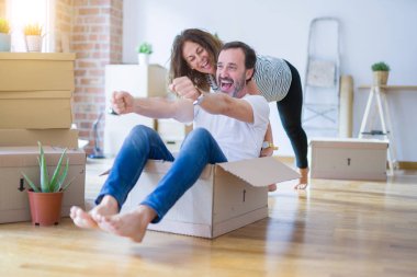Orta yaş üst düzey romantik çift, eğlenceli karton içinde sürme, heyecanlı ve yeni bir eve taşımak için mutlu gülümseyen
