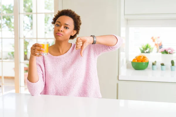 年轻的非洲裔美国女人满脸怒容地在家里滴橙汁 消极的迹象表明她不喜欢大拇指朝下 拒绝的观念 — 图库照片