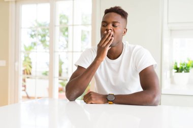 Yakışıklı afro-amerikan adam evde beyaz masada el ile ağız kapsayan yorgun esneme sıkılmış. Huzursuz ve uykululuk.