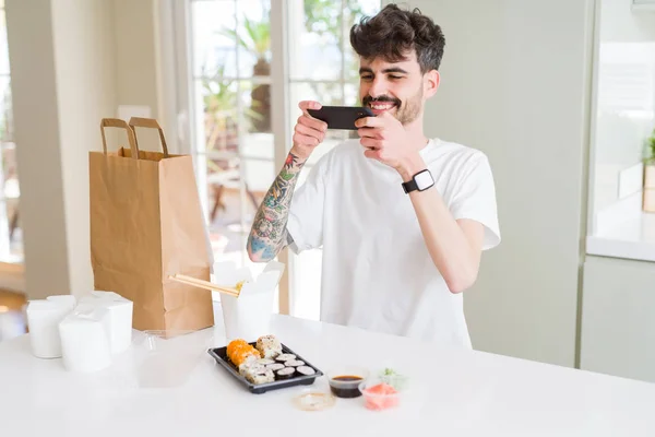 Young man taking pictures with smartphone of sushi asian food fr