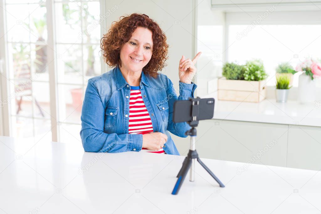 Senior woman doing video chat using smartphone camera with a big smile on face, pointing with hand and finger to the side looking at the camera.