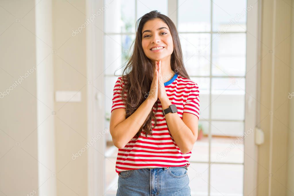 Young beautiful woman wearing casual t-shirt praying with hands together asking for forgiveness smiling confident.