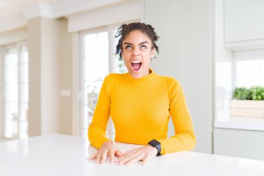 Afro saçlı güzel afro-amerikan kadın rahat bir sarı kazak giyen kızgın ve öfkeli çığlık sinirli ve öfkeli, öfke ile bağırarak. Öfke ve agresif kavram.