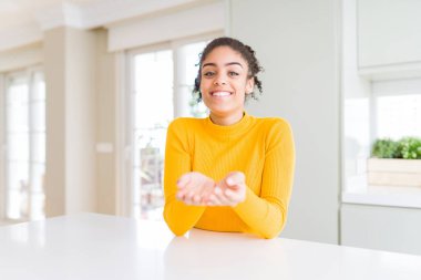 Afro saçlı güzel afro-amerikan kadın rahat sarı bir kazak giyen birlikte alma veya jest veren avuç içi ile gülümseyerek. Tutma ve koruma