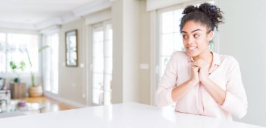 Wide angle of beautiful african american woman with afro hair laughing nervous and excited with hands on chin looking to the side