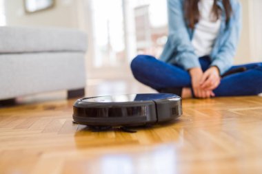Yerleri temizlemek için otomatik süpürge kullanan genç bir kadın makine ev işi robotu kontrol ediyor.