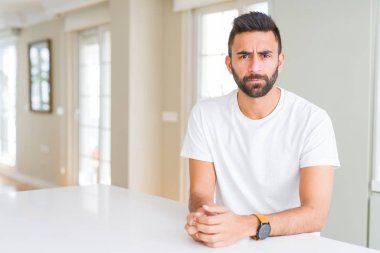 Yakışıklı İspanyol adam evde rahat beyaz t-shirt depresif ve sıkıntı için endişe, kızgın ve korkmuş ağlıyor. Hüzünlü ifade.