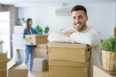 Genç çift yeni bir ev, yakışıklı adam karton kutular üzerinde eğilerek gülümseyen hareket