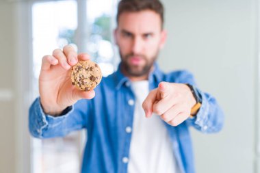Yakışıklı adam kamera ve size parmak ile işaret çikolata cips çerezleri yeme, el işareti, önden olumlu ve kendinden emin jest