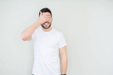Gülümsüyor ve gözleri için sürpriz kapsayan yüz el ile gülüyor izole arka plan üzerinde rahat beyaz t-shirt giyen genç yakışıklı adam. Kör kavramı.