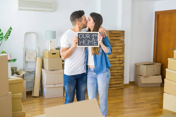 Beautiful young couple moving to a new house, smiling very happy holding blackboard with our first home text