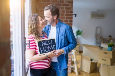Orta yaş Senior çift yeni bir eve hareket, yeni bir ev metin ile bir tahta tutan Apartmant aşık mutlu gülümseyen