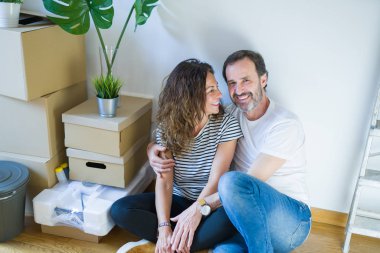 Orta yaş üst düzey romantik çift etrafında karton kutular ile daire katında oturan ve yeni bir eve taşınmak için mutlu gülümseyen aşk