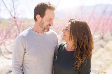 Baharın güneşli bir gününde pembe yaprakları ile şeftali ağaçlarının romantik bahçesinde aşık gülümseyen güzel orta yaş yaşlı çift