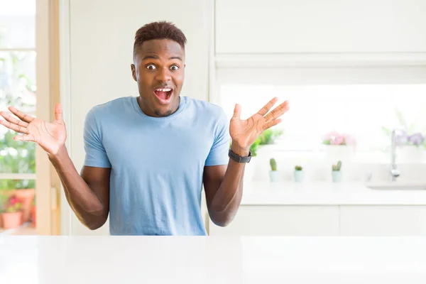 自宅でカジュアルなTシャツを着たハンサムなアフリカ系アメリカ人男性は 腕を上げて目を開けて興奮して成功に驚きました 勝者のコンセプト — ストック写真