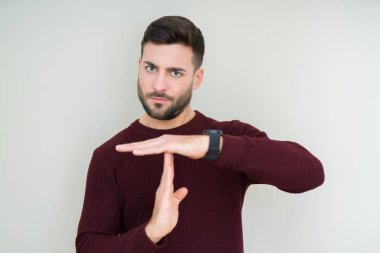 Soyutlanmış arka planda süveter giyen genç yakışıklı bir adam elleriyle jest yapıyor, hayal kırıklığına uğramış ve ciddi bir yüz ifadesi takınıyor.