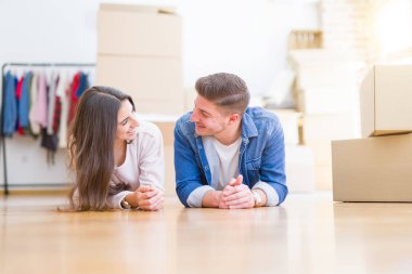 Evde karton kutular etrafında yerde yatan rahatlatıcı genç güzel çift, yeni bir eve hareket mutlu gülümseyen