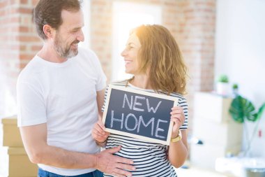 Orta yaş Senior çift yeni bir eve hareket, yeni bir ev metin ile bir tahta tutan Apartmant aşık mutlu gülümseyen