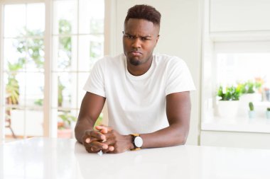 Yakışıklı afro-amerikan adam evde beyaz masada depresif ve sıkıntı için endişe, kızgın ve korkmuş ağlıyor. Hüzünlü ifade.