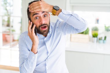 Yakışıklı İspanyol iş adamı akıllı telefon üzerinde konuşurken bir konuşma yaparken el ile stresli baş, utanç ve sürpriz yüz ile şok, kızgın ve sinirli. Korku ve hata için üzgün.