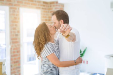 Orta yaş Senior romantik çift tutan ve ev anahtarlarını gösteren, sarılmak ve yeni bir eve taşımak için mutlu gülümseyen