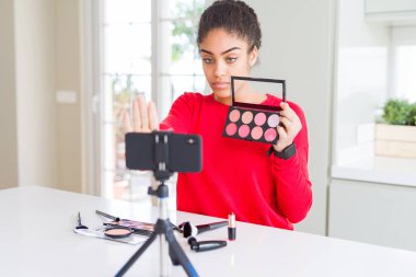 Genç afro-amerikan influencer kadın kayıt ciddi ve kendinden emin ifade, savunma jesti ile dur işareti yapıyor açık el ile öğretici makyaj