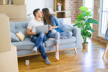 Genç çift yeni bir ev bilgisayar laptop kullanarak kanepede oturan rahatlatıcı, yeni daireye taşımak için mutlu gülümseyen hareket