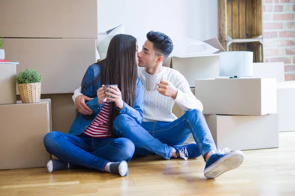 Young asian couple sitting on the floor of new house arround cardboard boxes relaxing from moving drinking a cup of coffe