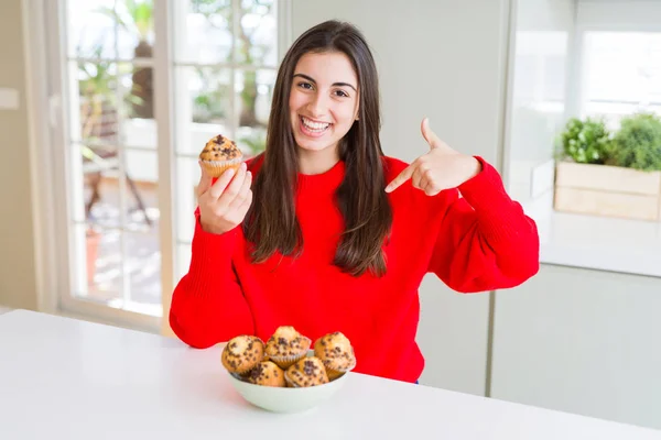 チョコレートチップマフィンを食べる美しい若い女性は 驚きの顔で自分自身に指を指さす — ストック写真