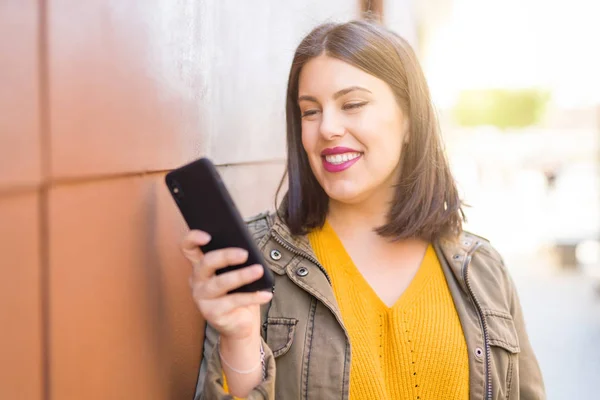 Krásná Mladá Žena Pozitivně Usmívá Pomocí Smarpthone Který Opírá Zeď — Stock fotografie