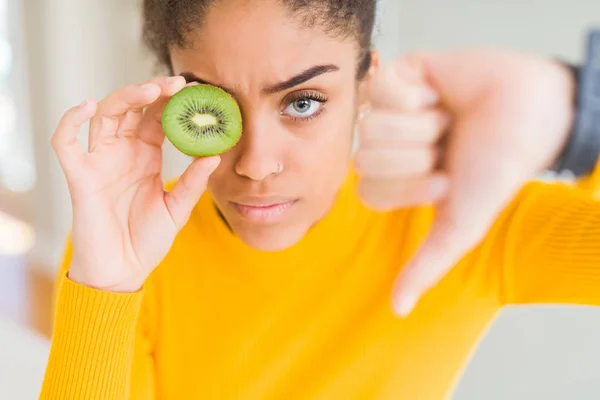 年轻的非洲裔美国女孩 满脸怒容地吃着绿猕猴桃 消极的迹象表明她不喜欢大拇指朝下 拒绝的观念 — 图库照片