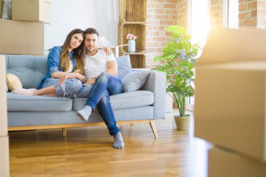 Young beautiful couple relaxing sitting on the sofa around boxes from moving to new house with serious expression on face. Simple and natural looking at the camera.