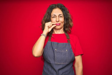 Kırmızı izole arka plan ağız ve dudaklar üzerinde önlük üniforma giyen orta yaş yaşlı kadın parmakları ile zip olarak kapattı. Gizli ve sessiz, tabu konuşma