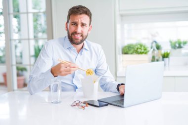 İş adamı yemek götürün Asya erişte yemek çalışma kullanırken bilgisayar dizüstü ve gülümseyen