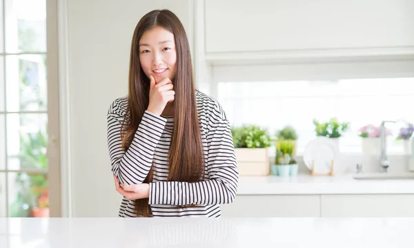 Beautiful Asian woman wearing stripes sweater looking confident at the camera with smile with crossed arms and hand raised on chin. Thinking positive.