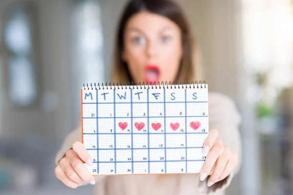 Young Beautiful Woman Holding Menstruation Calendar Home Scared Shock Surprise — Stock Photo, Image