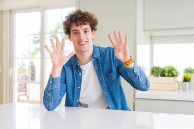 Evde rahat kot ceket giyen genç yakışıklı bir adam dokuz numaralı parmaklarıyla gösterip işaret ederken kendinden emin ve mutlu gülümsüyor..