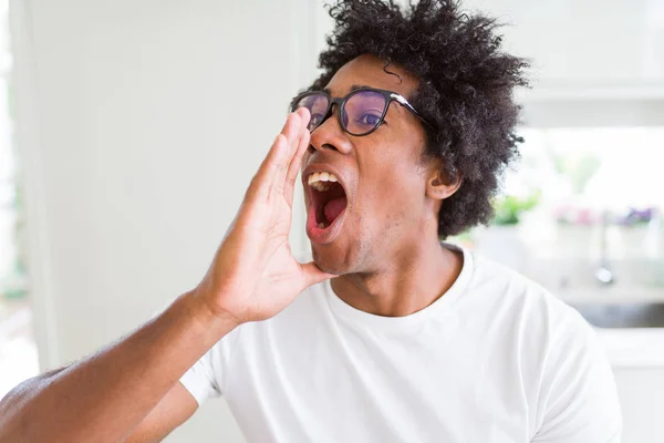 African American man wearing glasses shouting and screaming loud to side with hand on mouth. Communication concept.