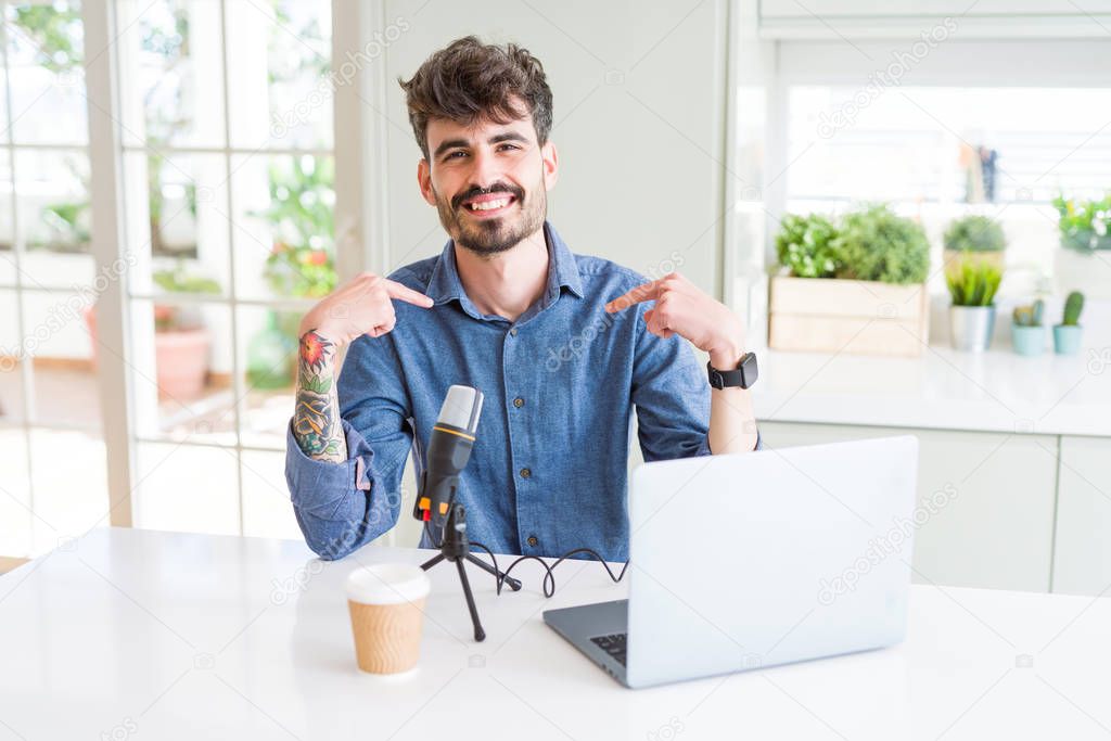 Young man recording podcast using microphone and laptop looking confident with smile on face, pointing oneself with fingers proud and happy.