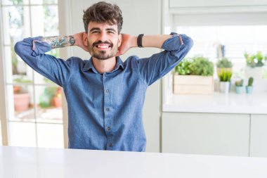 Beyaz masada oturan rahat gömlek giyen genç adam rahatlatıcı ve baş ve boyun arkasındaki silah ve eller ile germe, mutlu gülümseyen