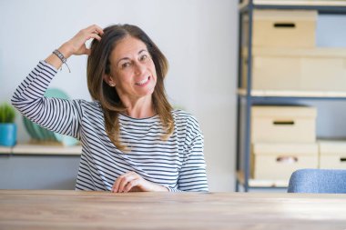 Orta yaş yaşlı kadın evde masada oturan kafa karıştırıcı ve soru hakkında merak. Şüpheyle belirsiz, eliyle kafada düşünmek. Pensive kavramı.
