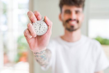 Genç adam mutlu bir yüz ayakta ve emin bir gülümseme dişleri gösteren ile gülümseyen kronometre tutarak kullanarak