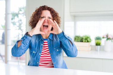 Evde kot ceket giyen kıvırcık saçlı orta yaş yaşlı kadın ağız üzerinde elleri ile öfkeli bağırıyor