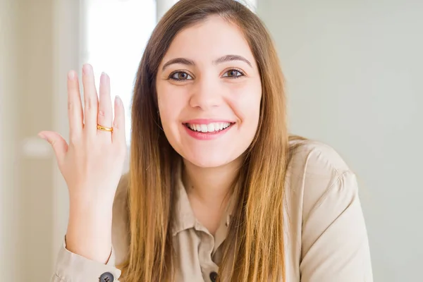 Beautiful young woman showing alliance ring on hand with a happy face standing and smiling with a confident smile showing teeth