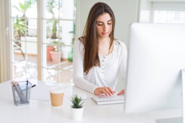 Bilgisayar kullanarak çalışan güzel genç iş kadını, gülümseyen ve online çalışma üzerinde konsantre