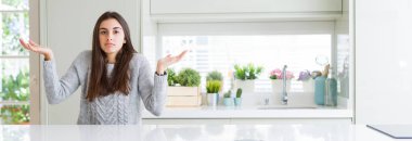 Beyaz ev clueless ve şaşkın bir ifadeyle kollar ve eller kaldırdı masada oturan güzel genç kadın geniş açı resim. Şüphe kavramı.