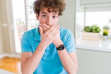 Evde rahat mavi t-shirt giyen genç yakışıklı adam yanlışlık için eller ile ağız kapsayan şok. Gizli konsept.