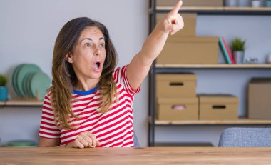 Orta yaş yaşlı kadın evde masada oturan parmak ile işaret önünde şaşırttı, açık ağız şaşkın ifade, ön bir şey